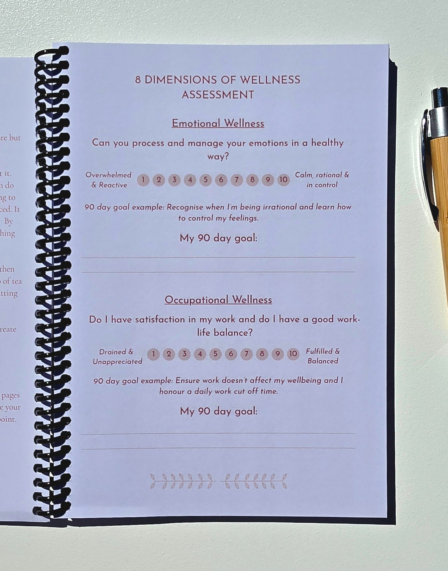 A spiral-bound notebook page titled '8 Dimensions of Wellness Assessment' with sections for Emotional and Occupational Wellness, photographed on a light surface with part of a pen visible on the right.