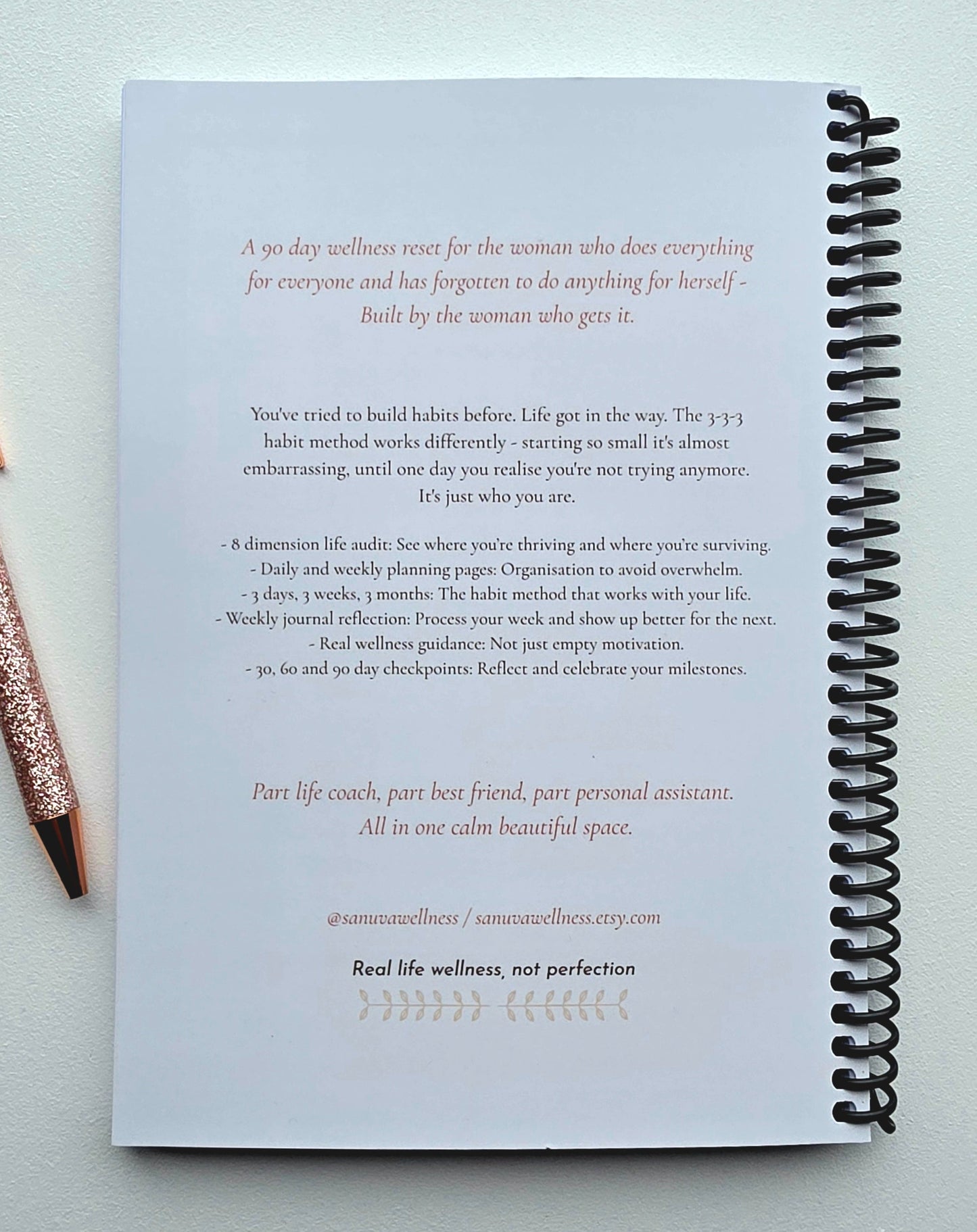 A spiral-bound notebook page with printed wellness text and a pink glitter pen resting on a light textured background.