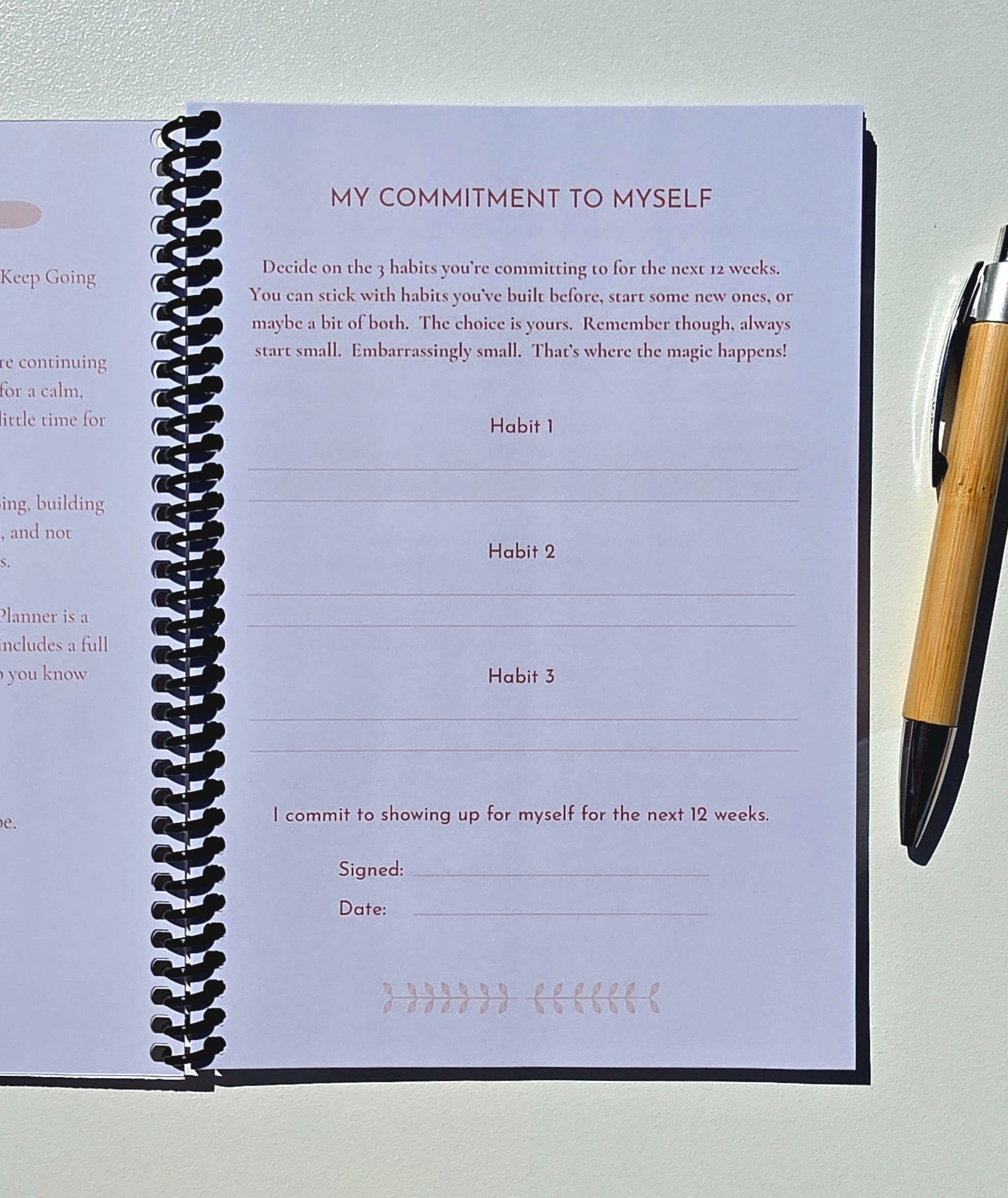 A spiral-bound journal or planner page showing a self-reflection commitment template titled 'MY COMMITMENT TO MYSELF' with habit lines, photographed on a light surface with a wooden pen beside it.