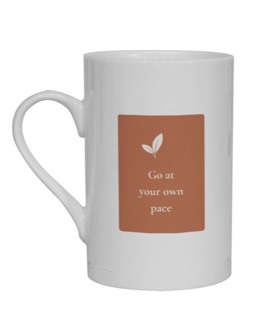 A white ceramic mug with a terrracots rectangular graphic on the front featuring a small leaf icon and the text 'Go at your own pace'.
