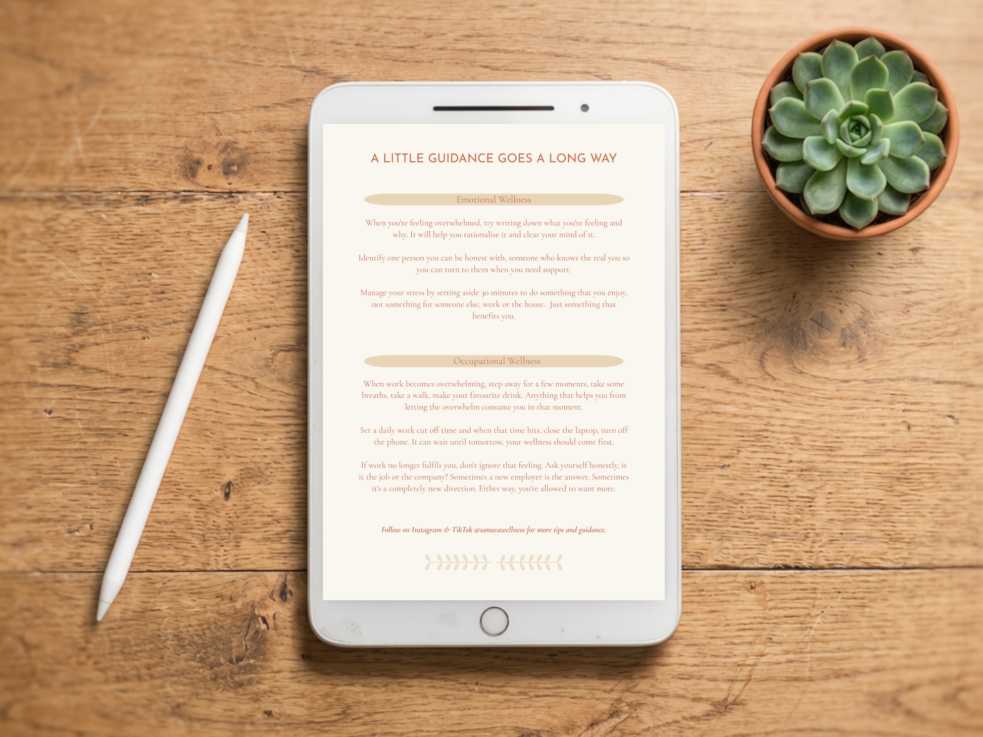 A tablet lying on a wooden tabletop, displaying a book or article page with the headline 'A LITTLE GUIDANCE GOES A LONG WAY.' A white stylus rests to the left, and a small potted succulent sits to the upper right.